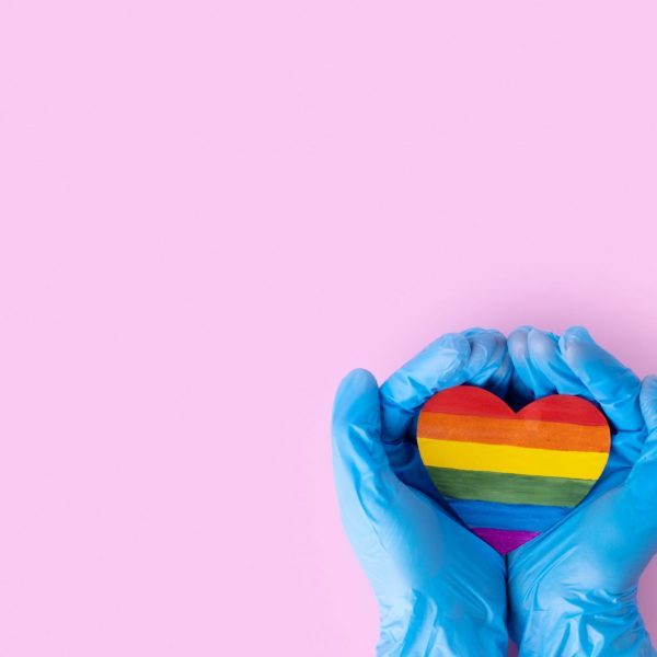 medical gloved hands holding rainbow paper heart